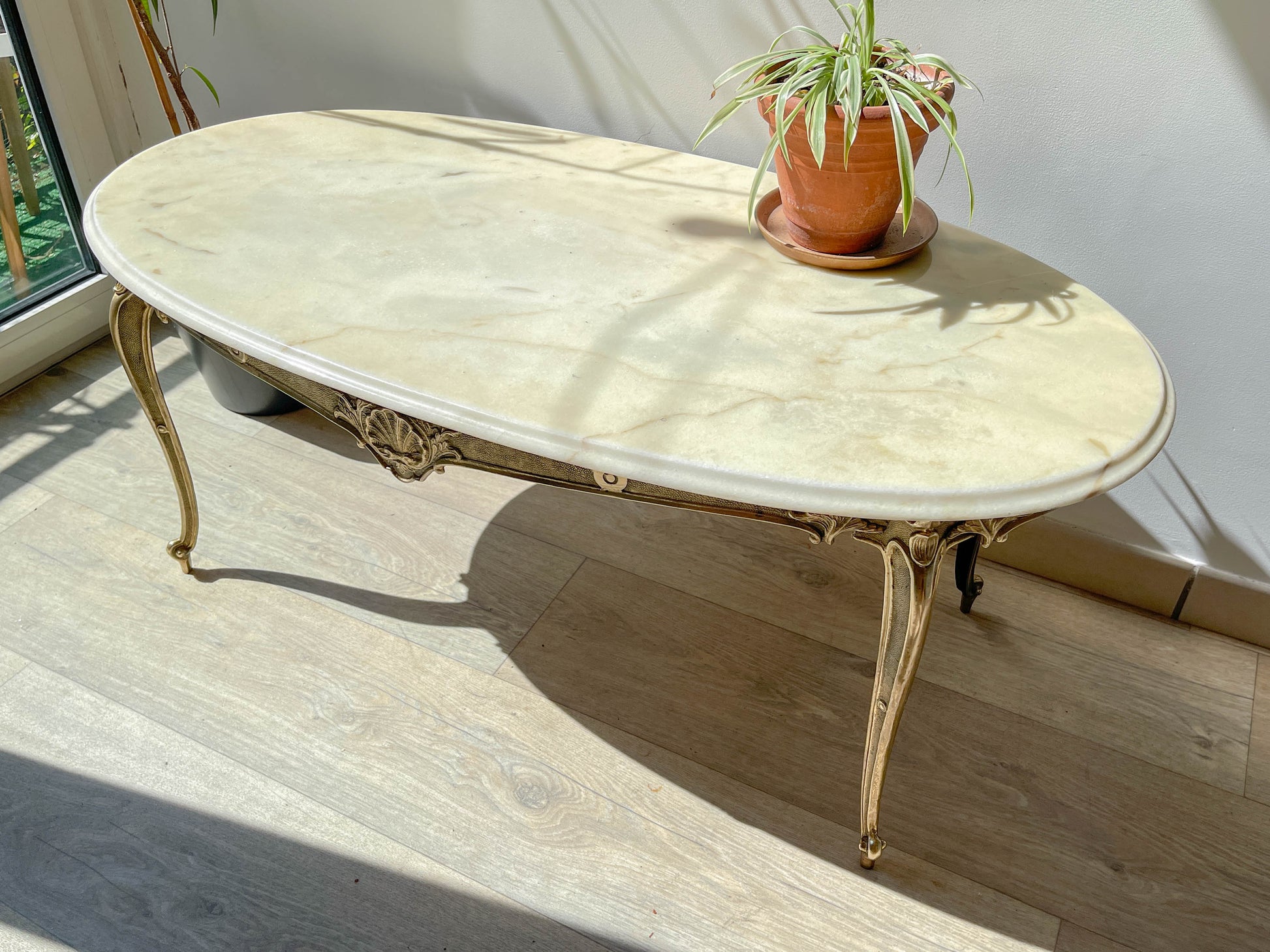 Table basse vintage ovale avec plateau en marbre blanc et pieds en bronze patiné, style chic et rétro pour salon.